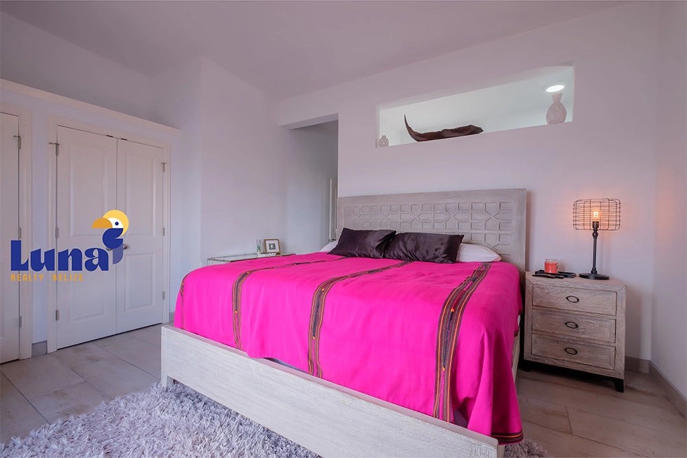 Bedroom with pink bedspread and nightstand lamp.