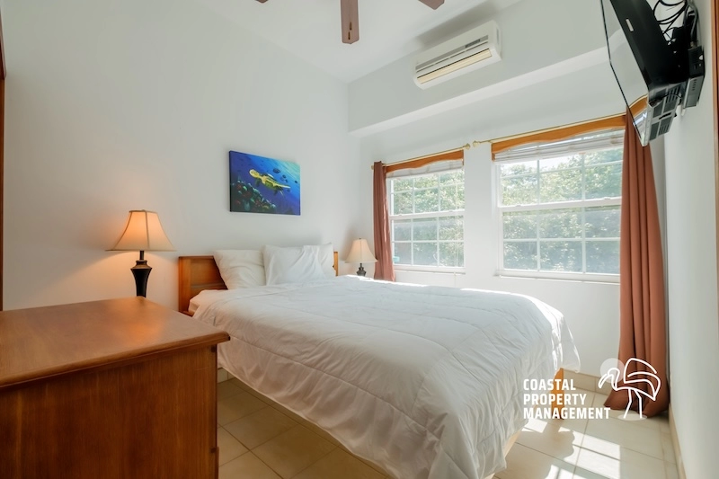 Bright bedroom with bed, dresser, and windows.