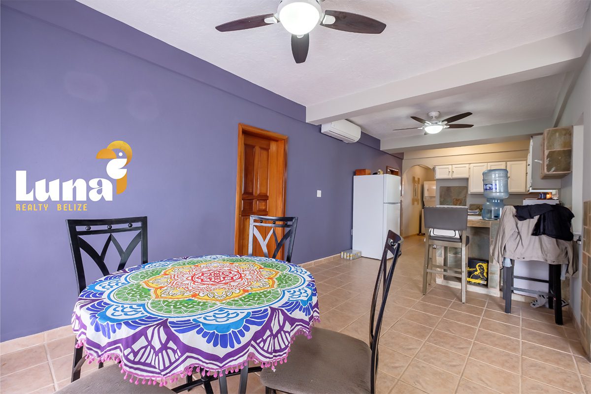 Dining area with colorful tablecloth and kitchen.