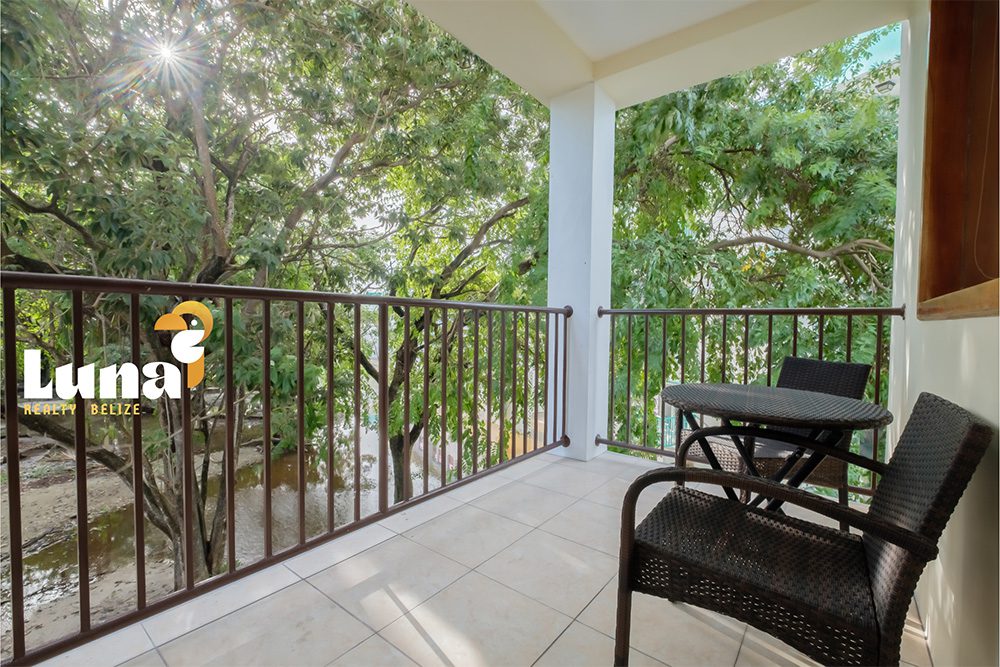 Balcony with chairs overlooking lush green trees.